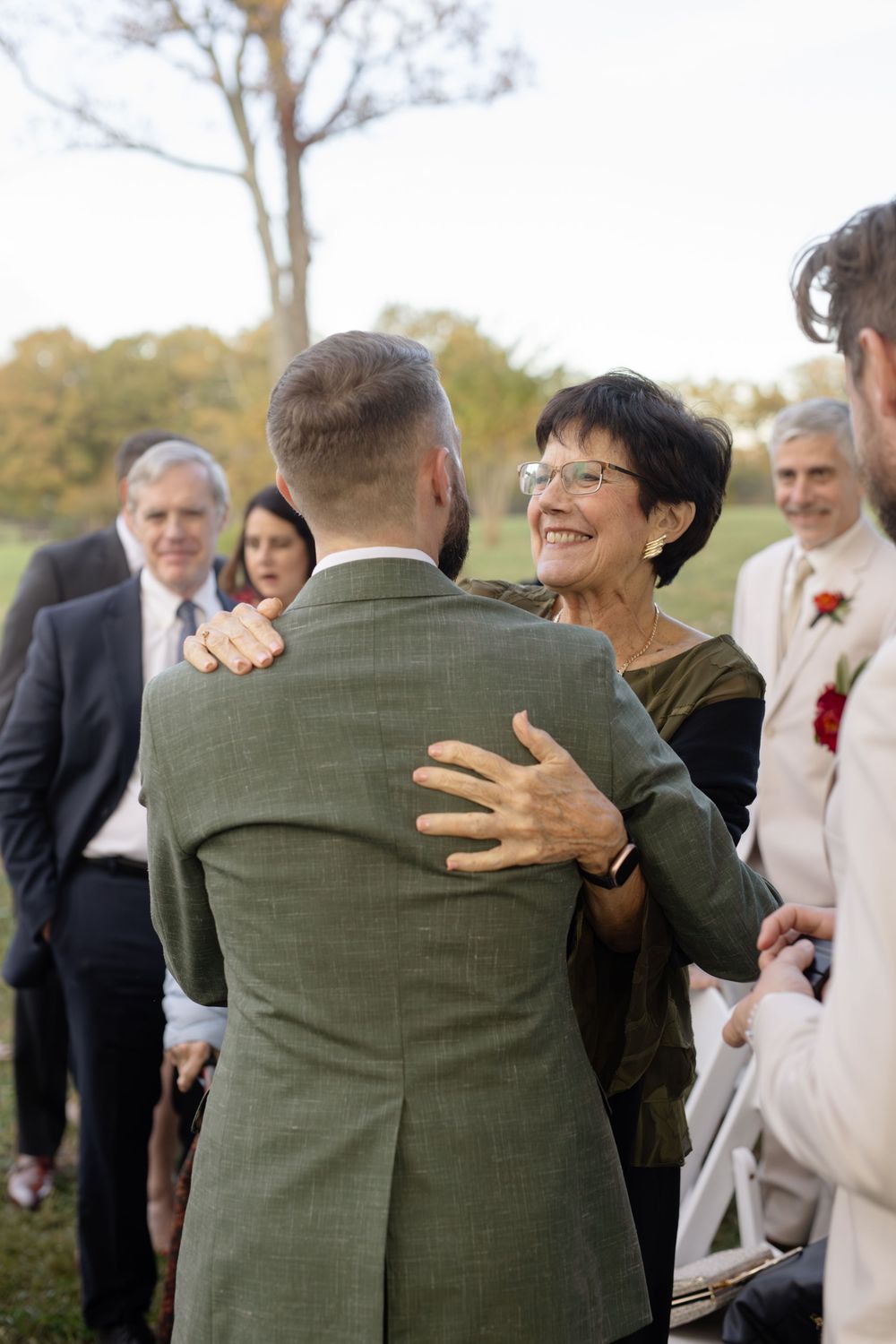 Wedding guests in formal attire embrace during an outdoor celebration.