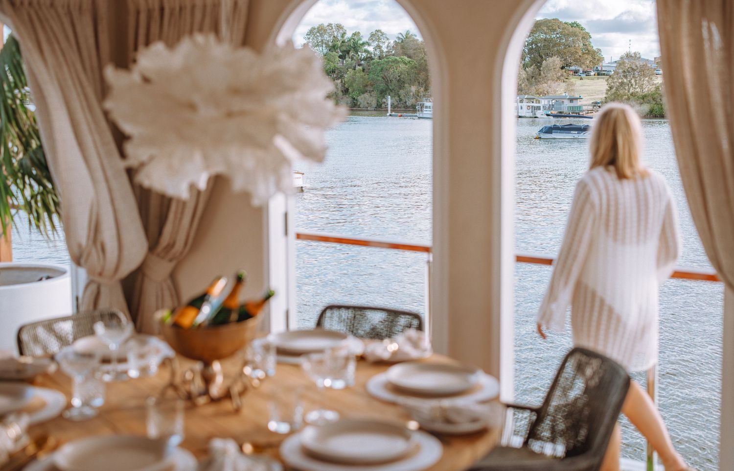 Elegant table setting with white decor and waterfront view through arched window.