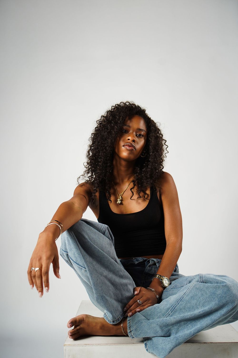 Person wearing black tank top and light blue jeans poses casually on white background in artistic portrait series.