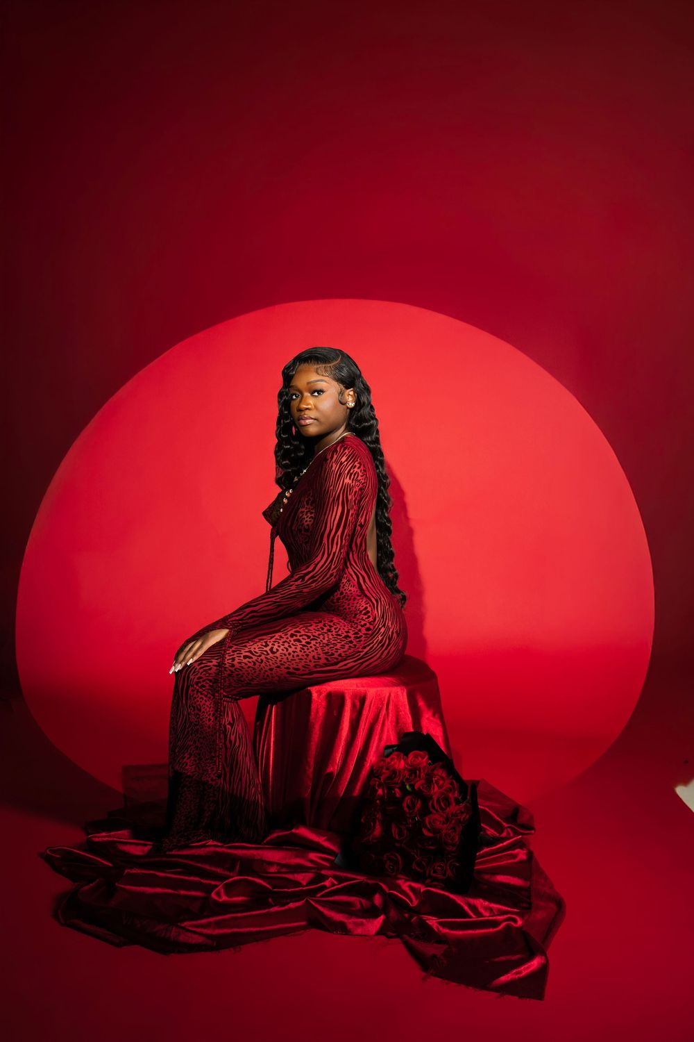 Figure in a sparkly red dress poses dramatically against a deep crimson backdrop in an artistic photo series.