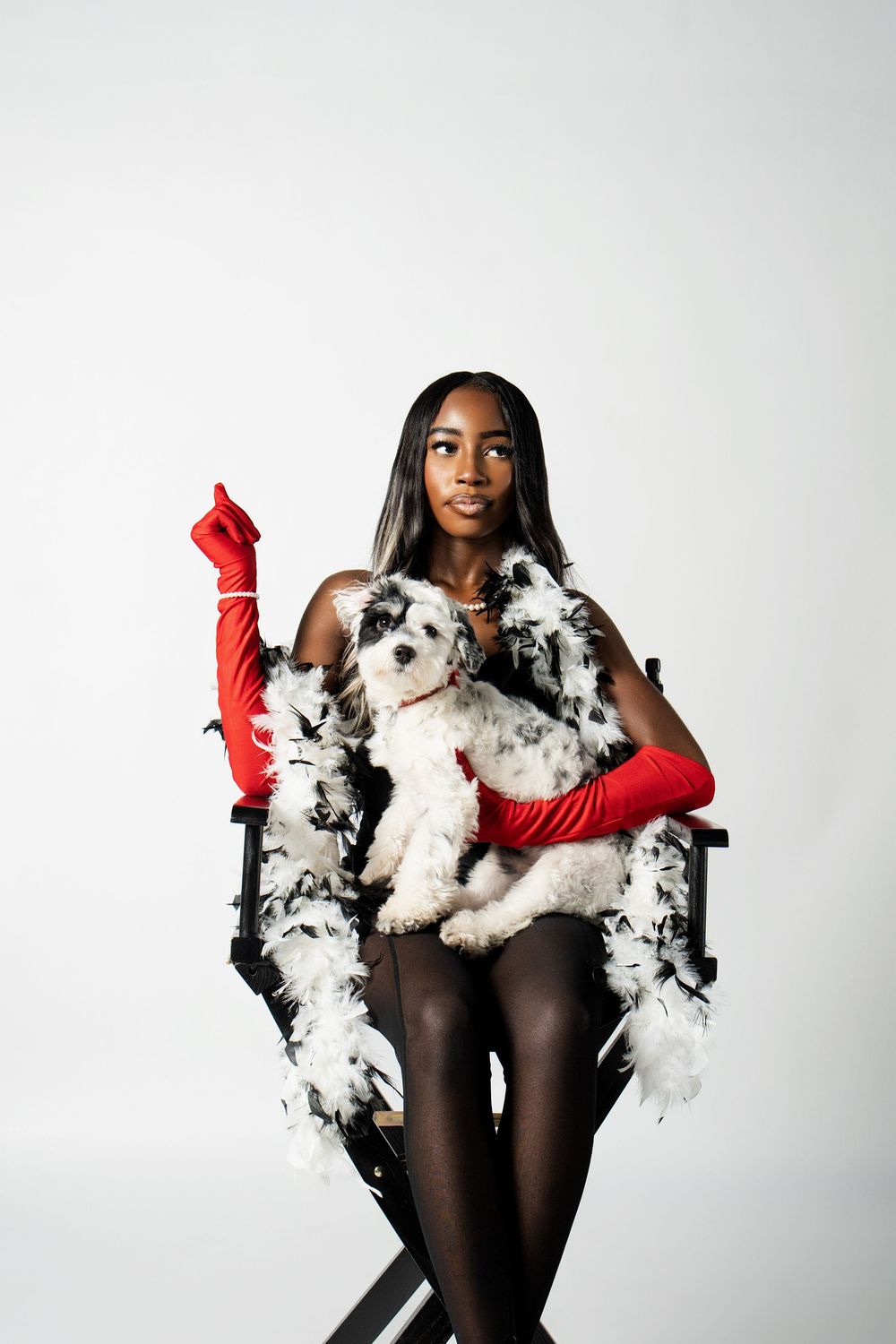 A model in black tights and red gloves poses with fluffy white dogs in a studio photoshoot series.