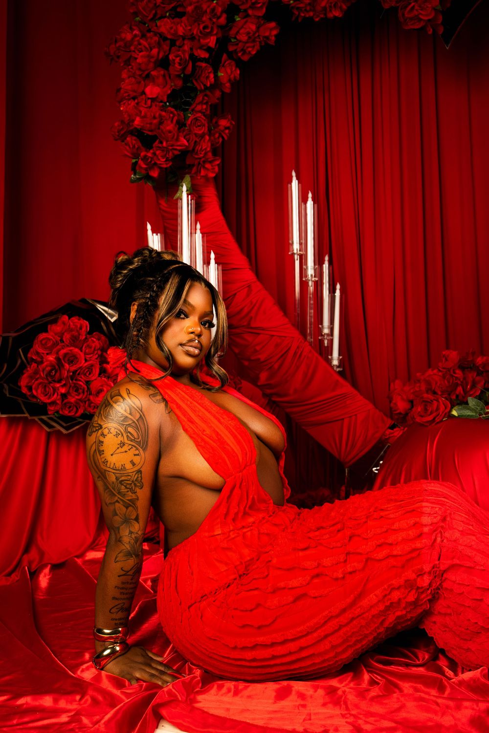 A person in a red dress poses seductively on red satin sheets in a dimly lit room with dramatic lighting.