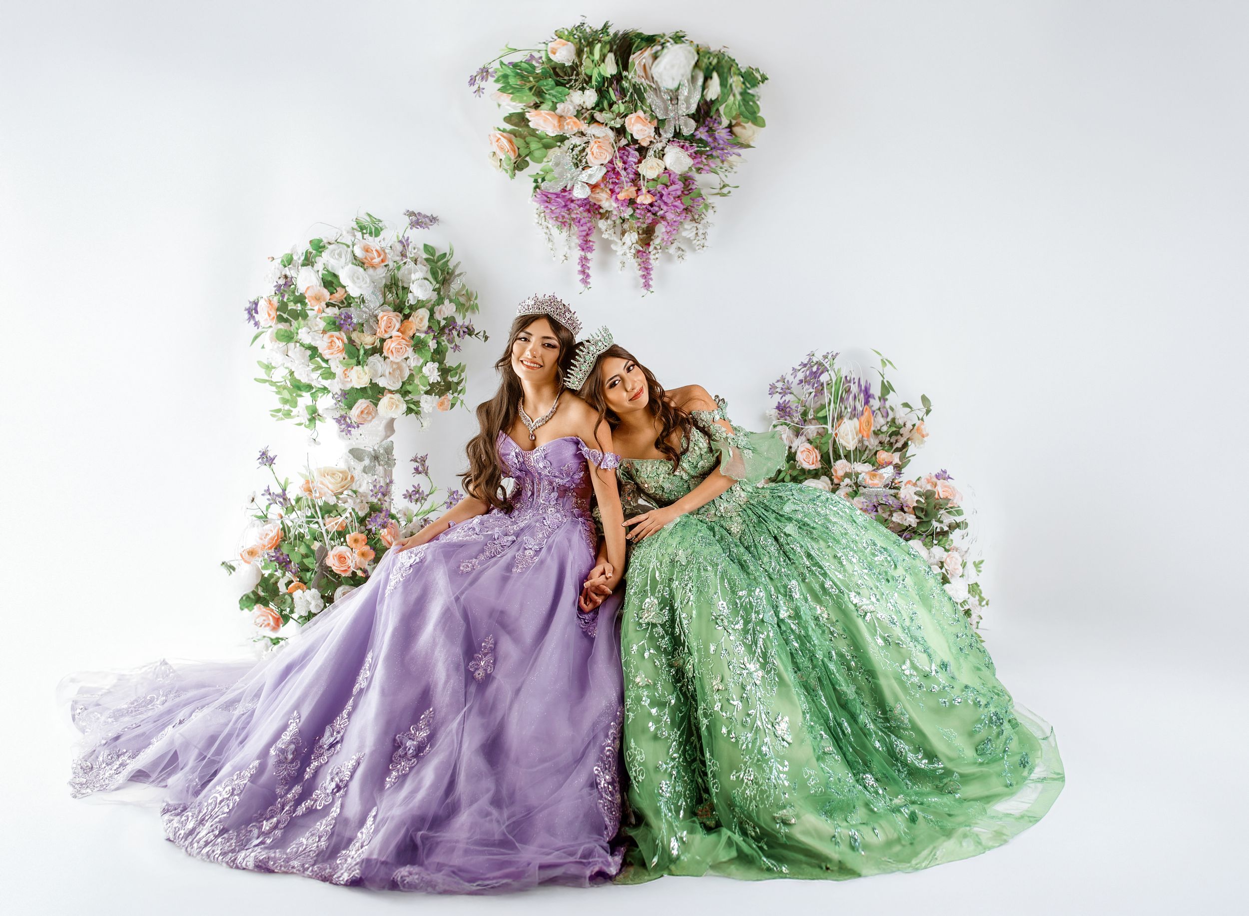 Two elegant ball gowns in mint green and lavender with floral accents create a dreamy fashion scene against white backdrop.