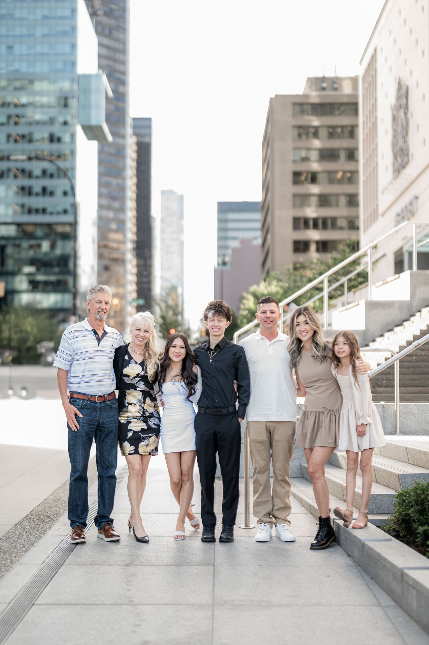 A group poses together on urban steps with modern buildings in the background for a casual outdoor photoshoot.