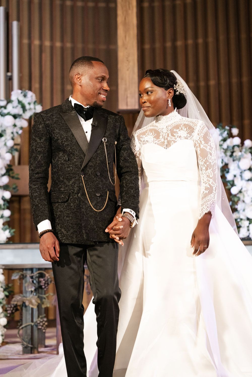 Wedding couple walking and posing together on wooden stage in formal attire.