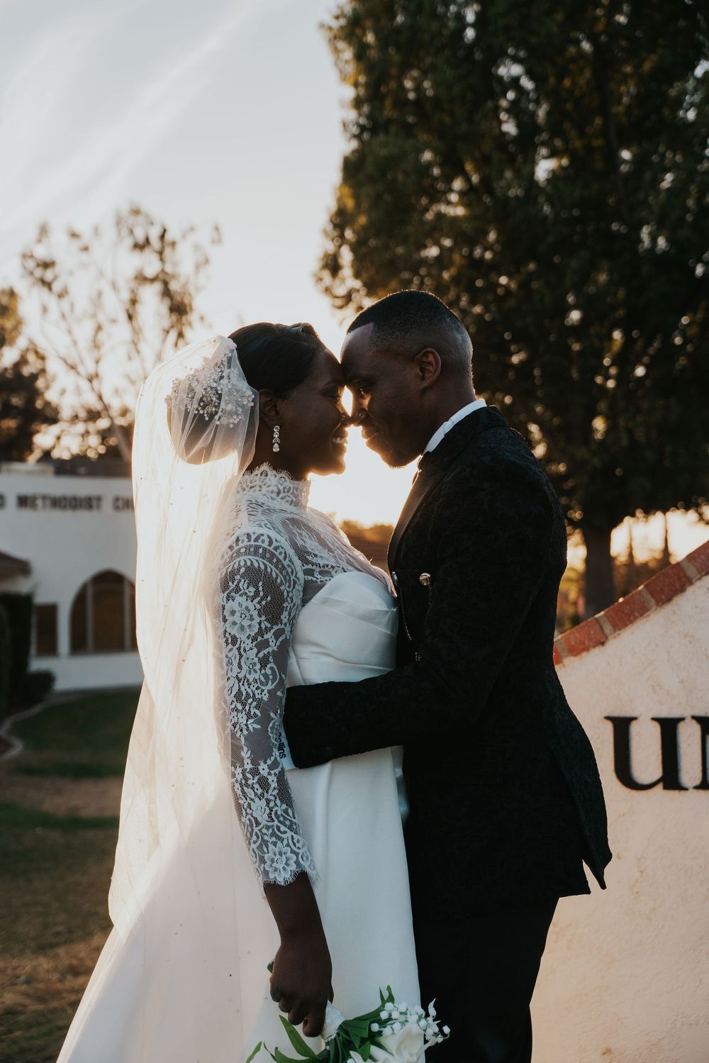 A romantic sunset wedding moment captured with a couple in an elegant white lace gown and black suit sharing an intimate pose.
