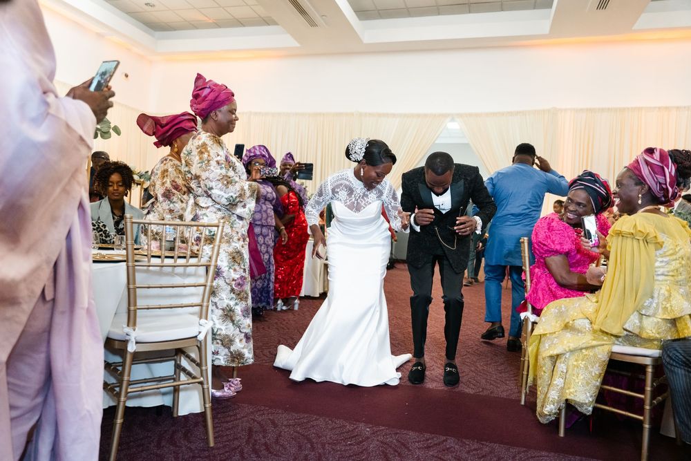 Wedding reception guests dancing and celebrating in an elegant banquet hall with gold chairs and decorative tables.