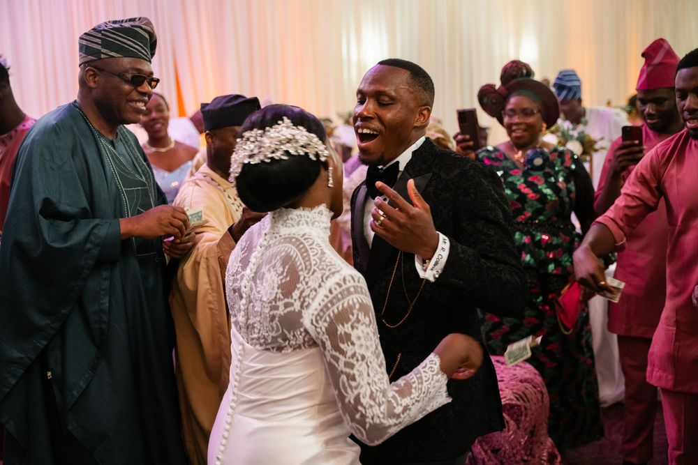 People dancing and celebrating at a wedding reception with pink lighting and festive atmosphere.