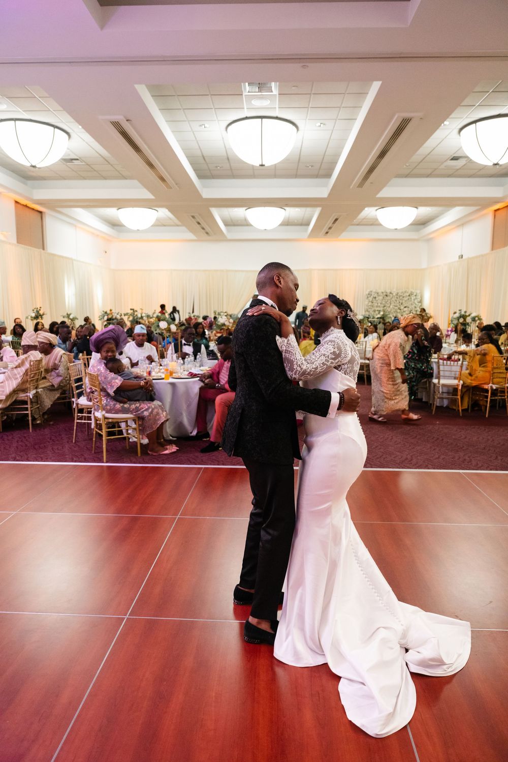 A romantic couple dances together at a wedding reception in an elegant ballroom with white decor and lighting.