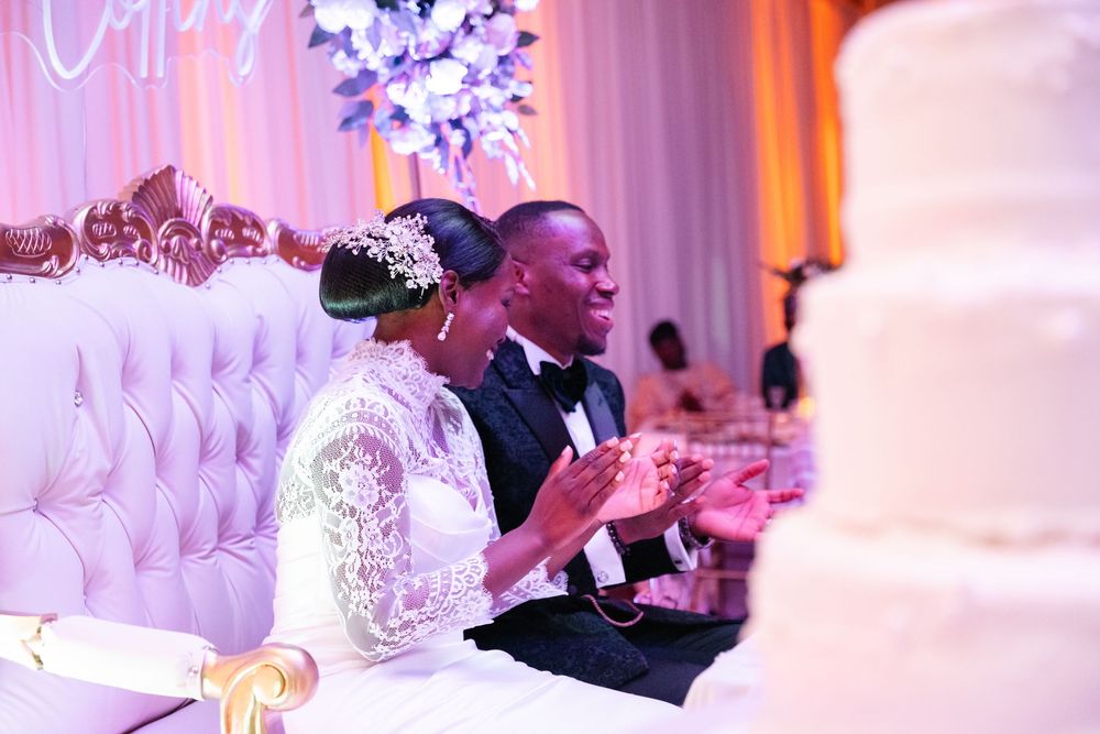 Wedding reception celebration with purple and pink lighting illuminating an elegant white decor setup at a grand venue.