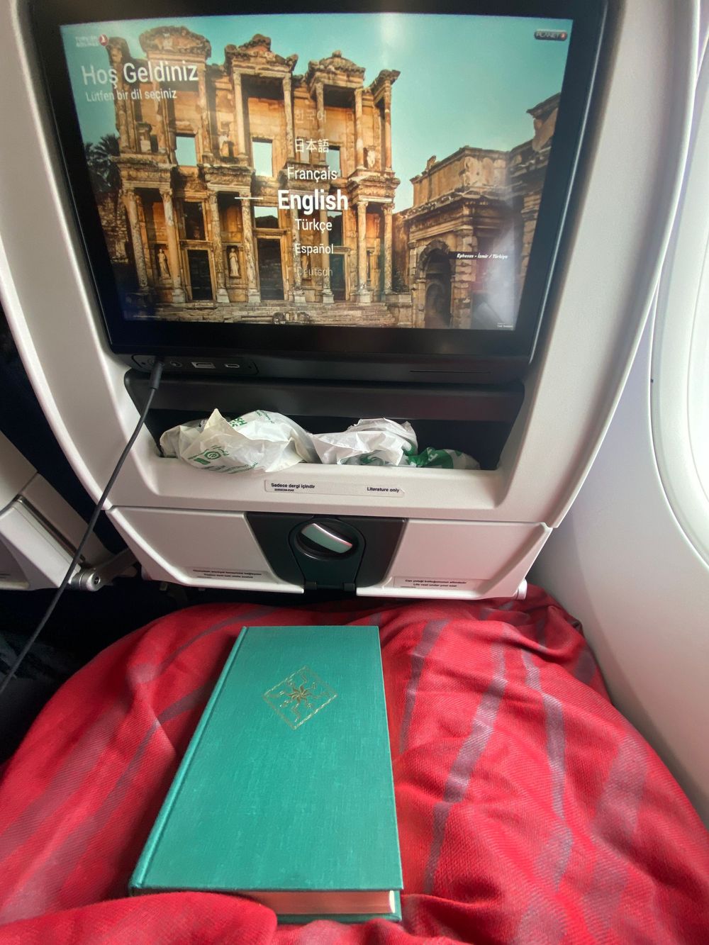 Airplane entertainment screens showing ancient ruins while green and red blankets rest on the seats below.