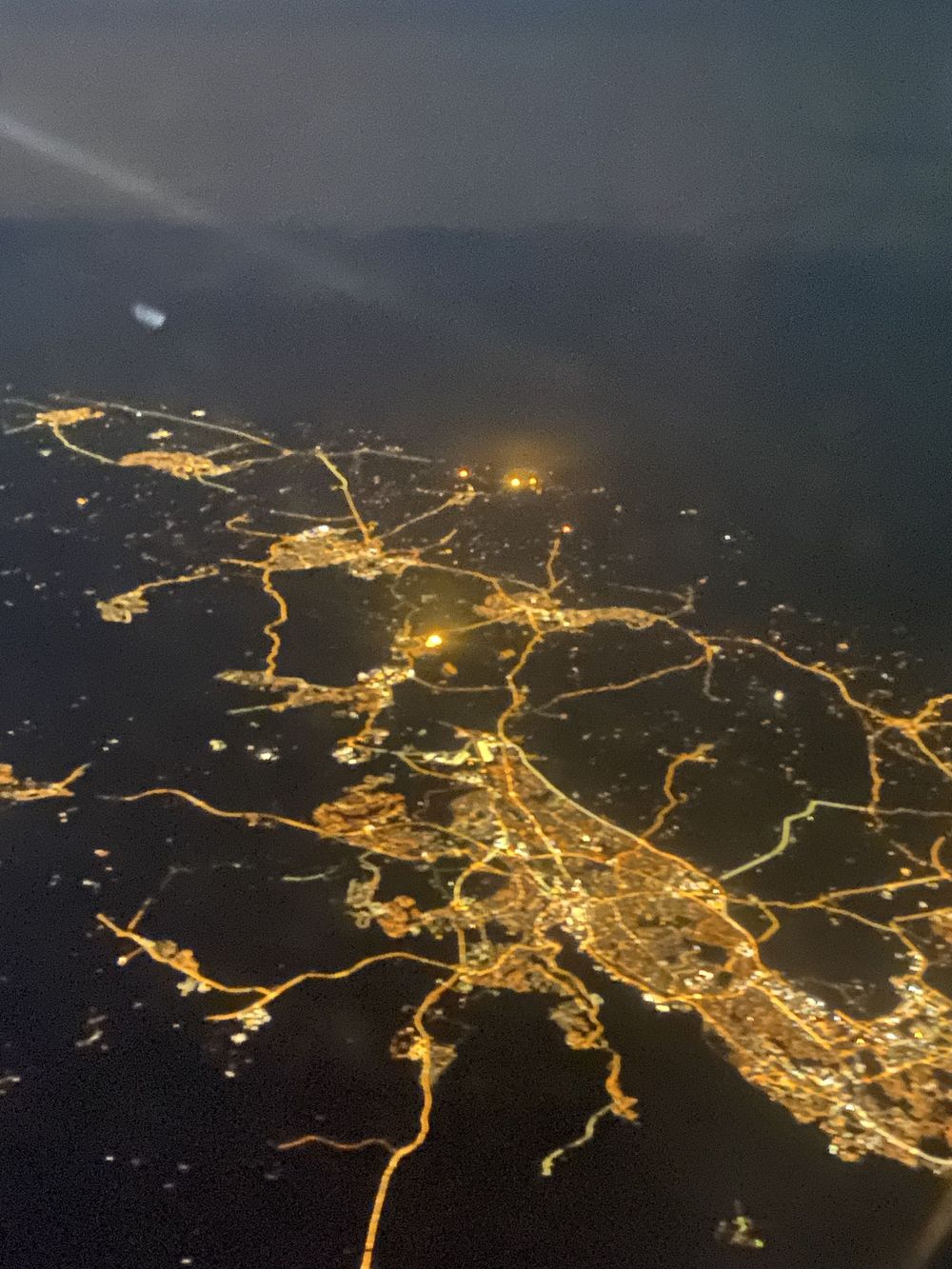 Aerial nighttime view of illuminated city streets and highways forming a glowing network pattern against dark terrain.