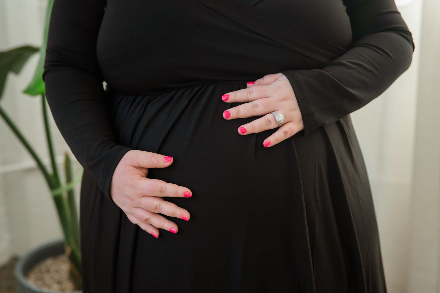 Close-up of hands gently cradling a pregnant belly while wearing a black maternity dress.