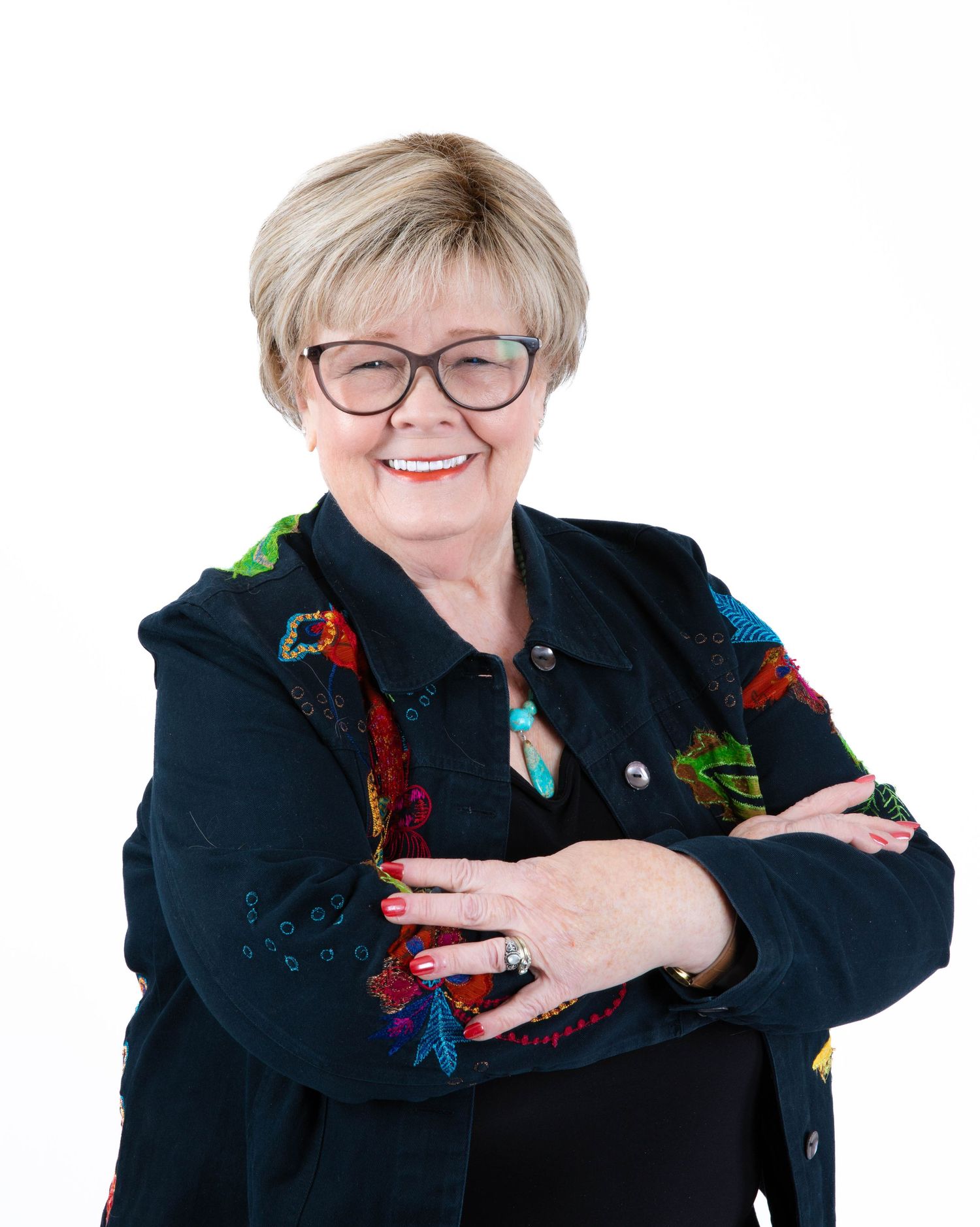 Professional portrait of someone wearing glasses and a black blazer with colorful embroidered details, smiling warmly.