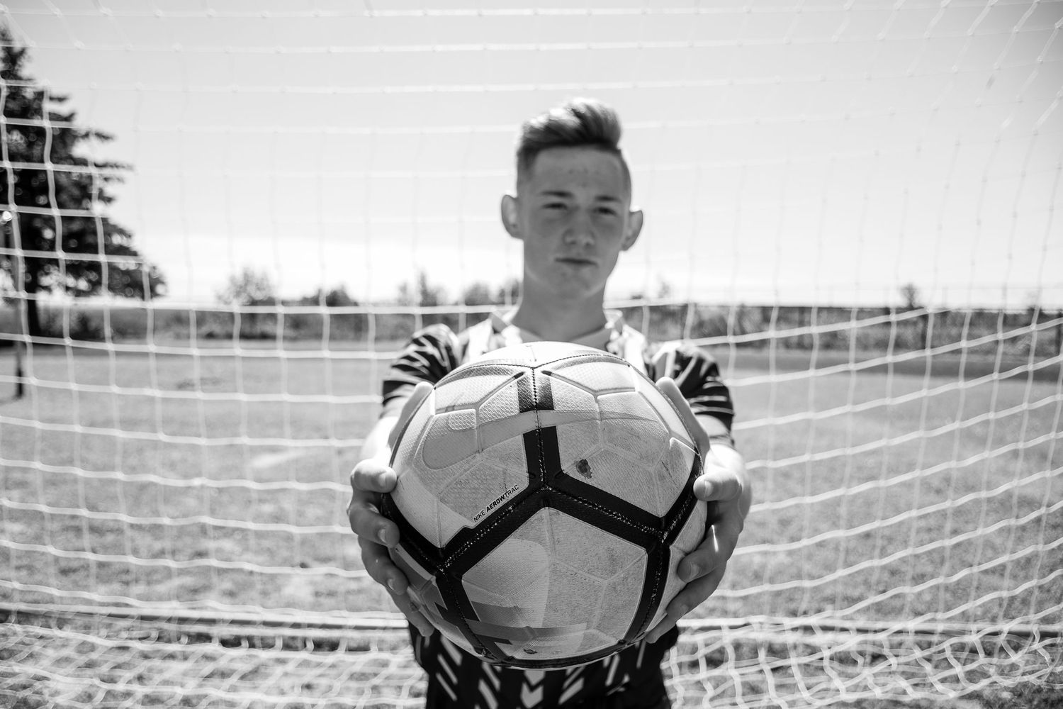 Black and white photo of a soccer goalkeeper holding a ball in front of a goal net.
