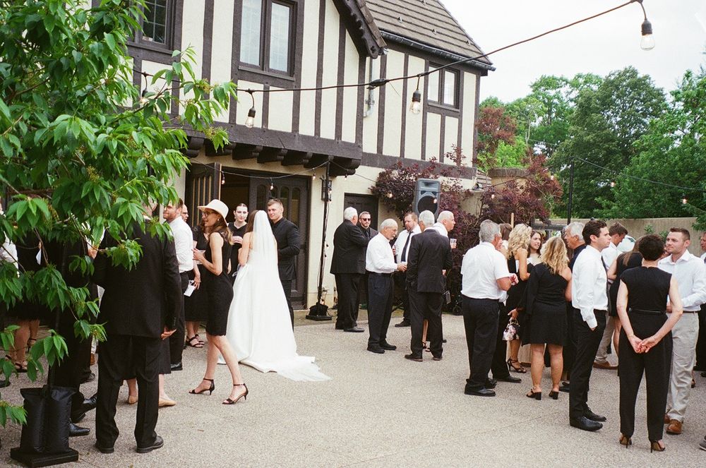 Wedding guests gather outside a Tudor-style building during an elegant outdoor reception celebration.