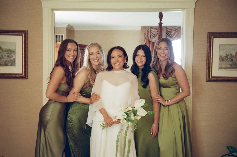 Bride in white gown with four bridesmaids in green dresses posing together in a doorway.