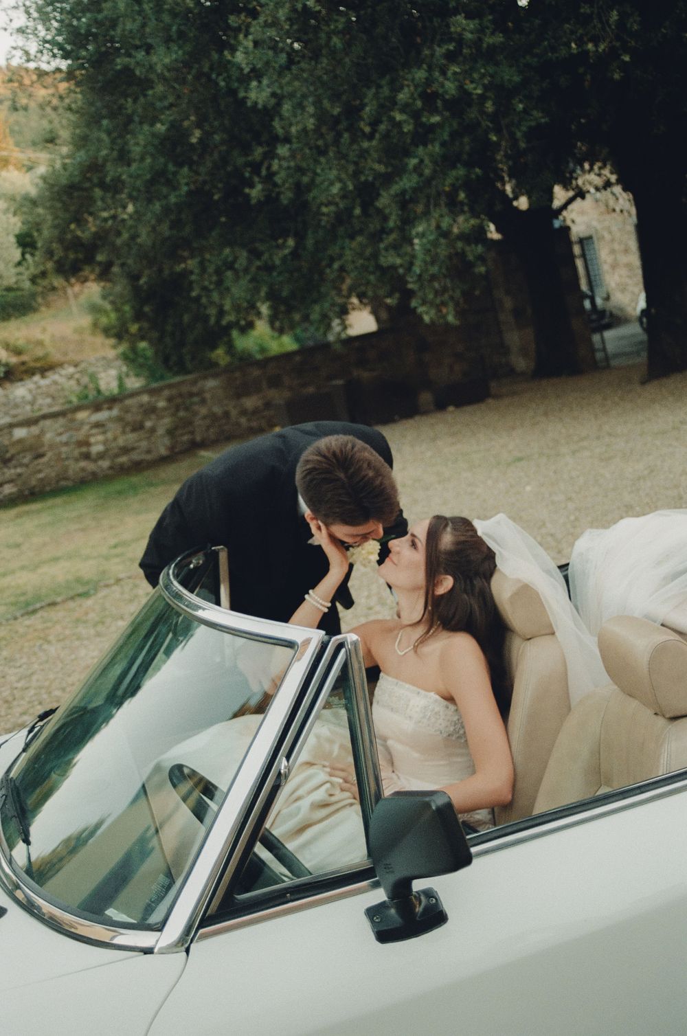 A romantic moment captured in a classic white convertible car against a natural outdoor backdrop.