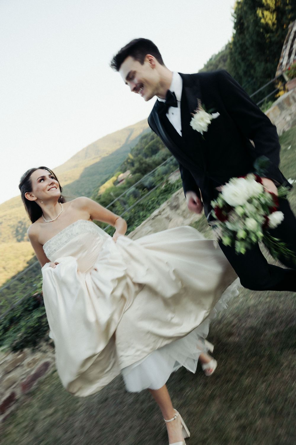 A bride and groom dance playfully in an outdoor setting with mountains visible in the background.