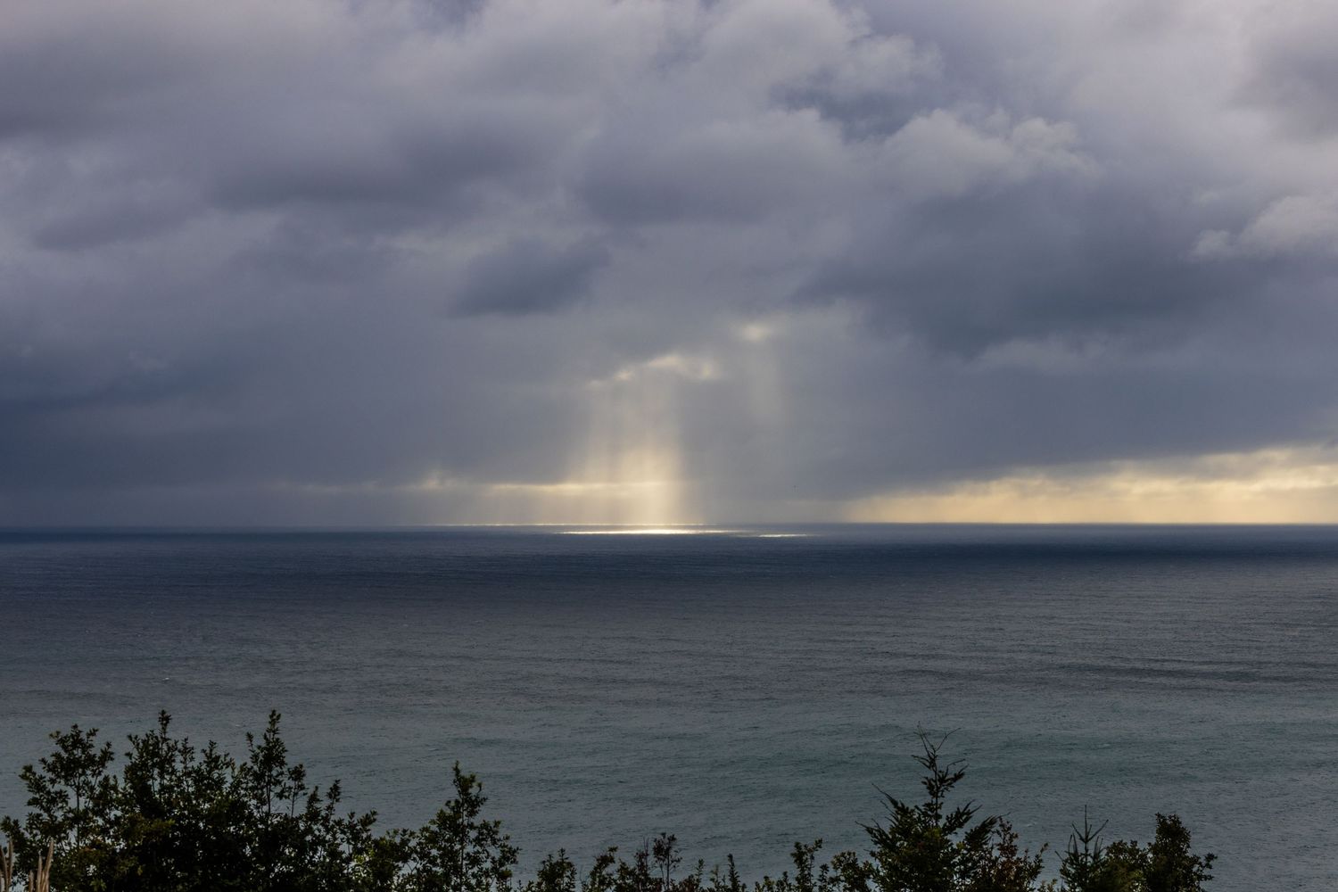 Dramatic storm clouds over the ocean with sunlight breaking through creating bright beams on the water's surface.