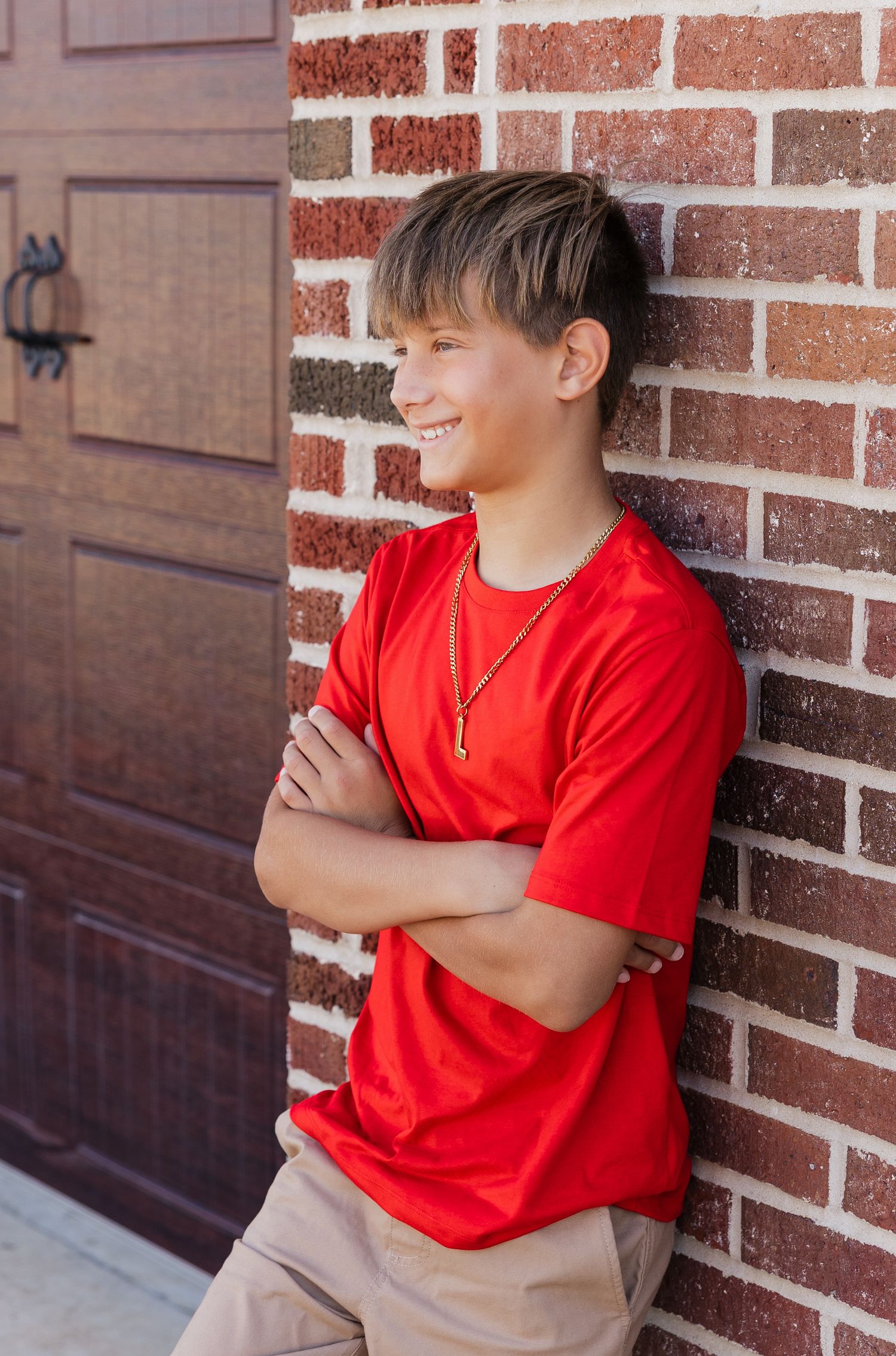 Young child in a red t-shirt and khaki shorts sits against a brick wall looking to the side.