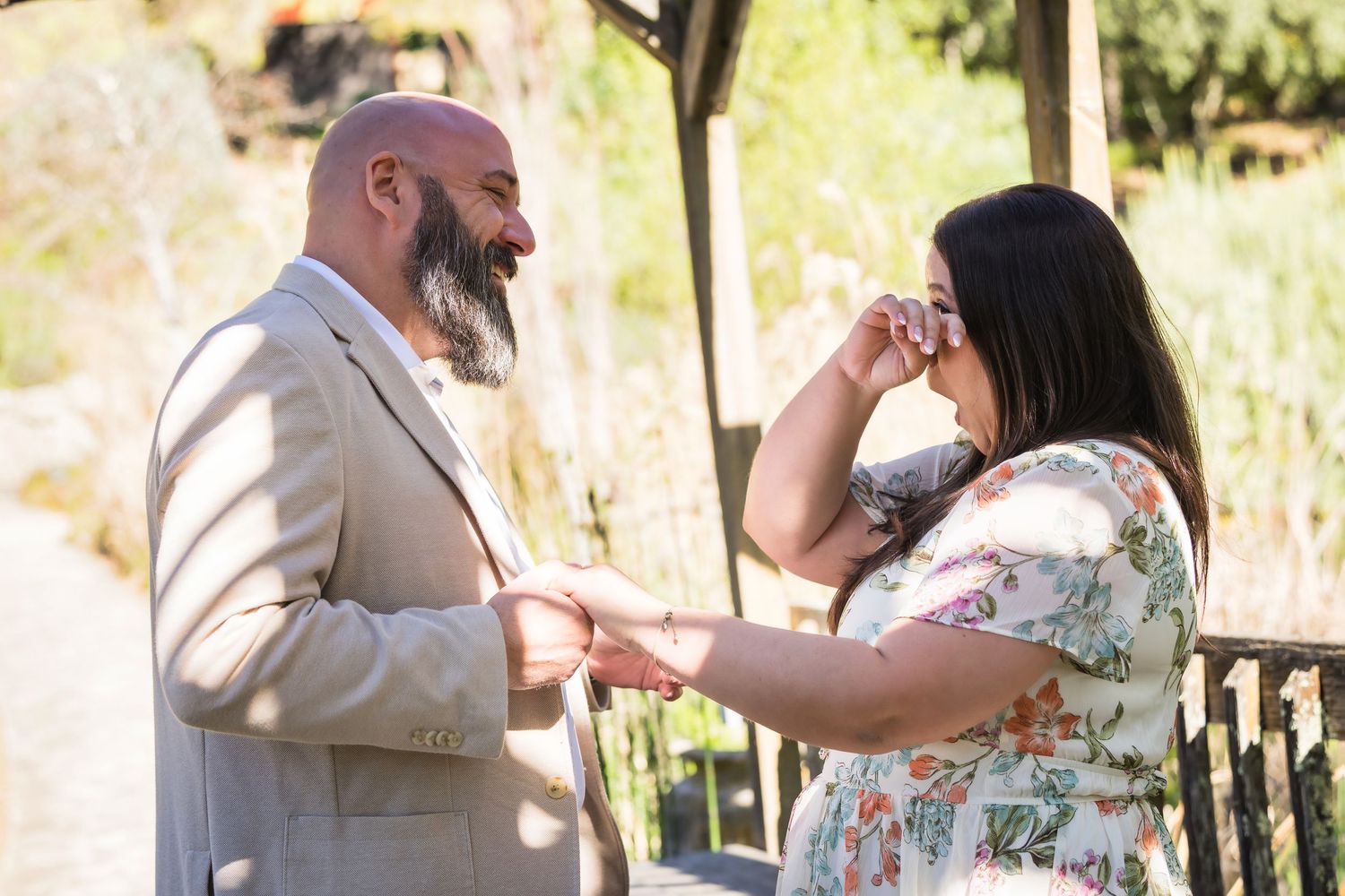 A couple celebrates during an outdoor wedding ceremony with sunlight filtering through trees in the background.