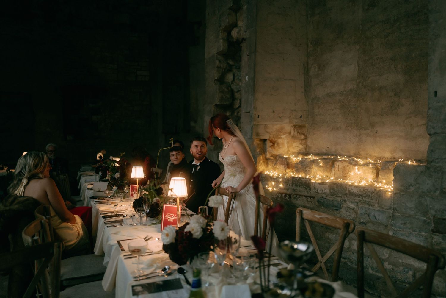 People gather for an intimate candlelit dinner at a rustic stone-walled venue with warm ambient lighting.