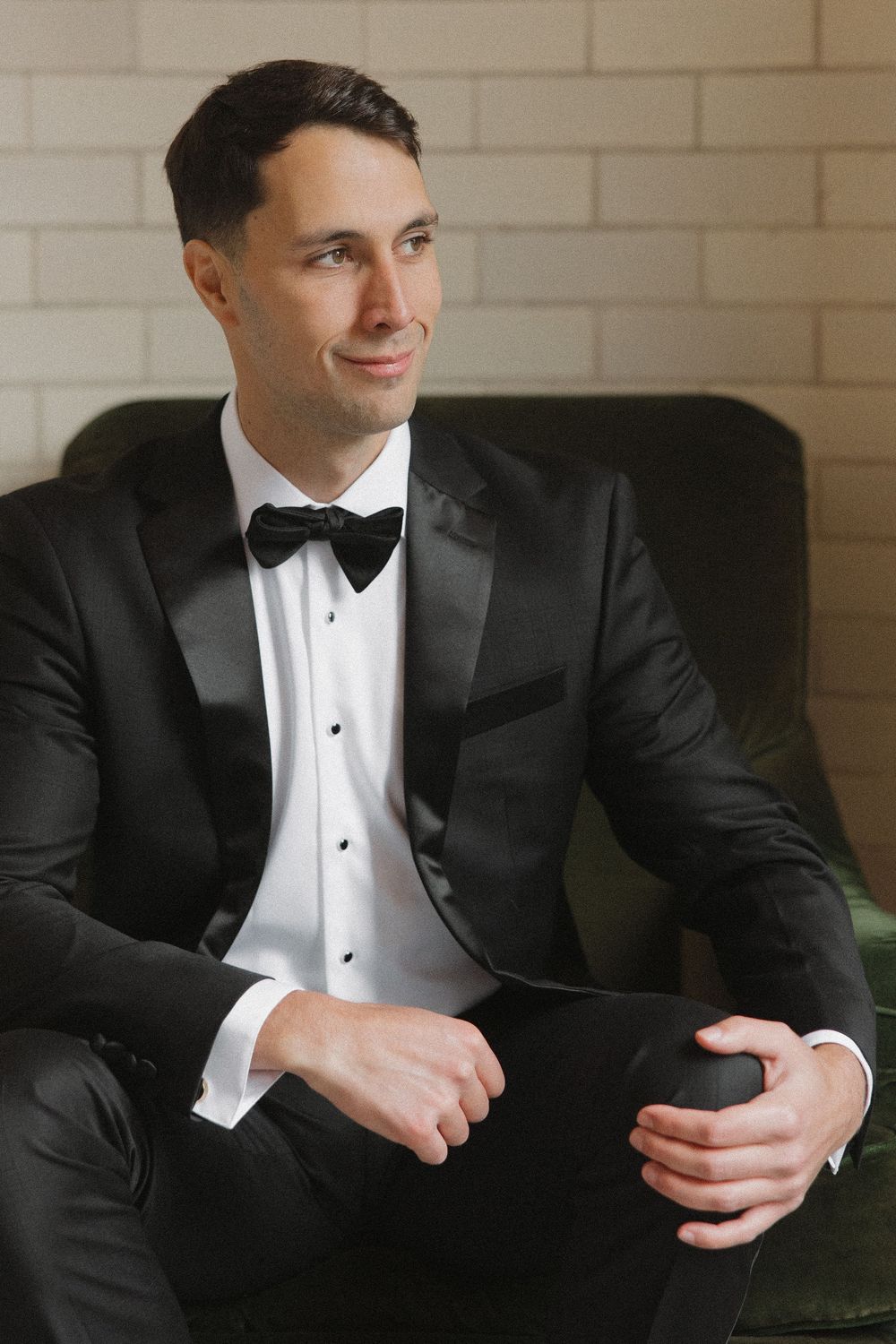 Close-up portrait series of someone in a classic black tuxedo with white shirt and bow tie sitting on green furniture.