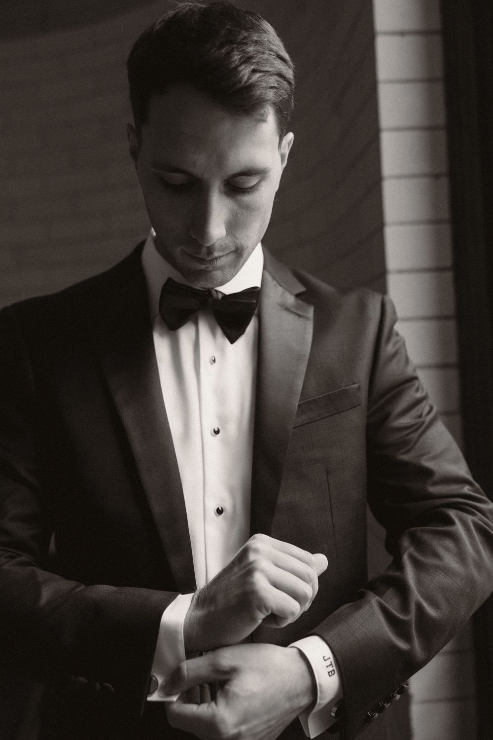 Moody black and white portrait of someone adjusting their formal tuxedo bow tie.