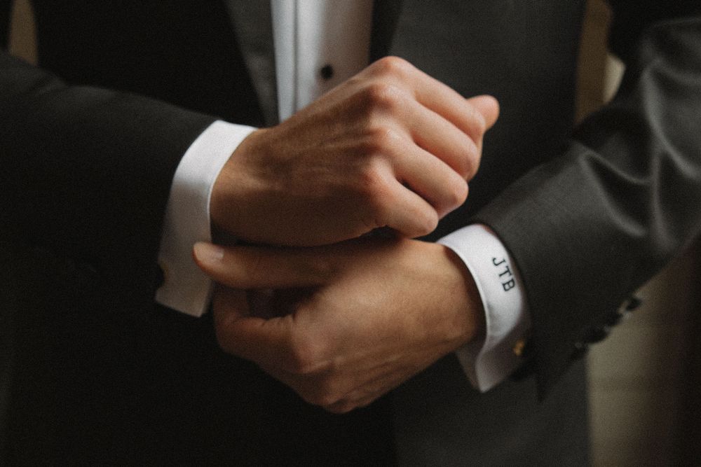 Professional close-up shot of hands adjusting a black suit sleeve with white shirt cuff visible.