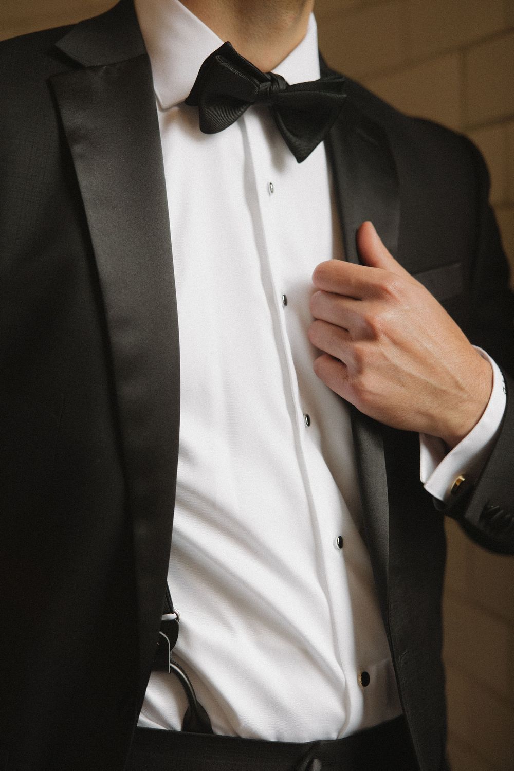 Close-up detail of a black tuxedo with bow tie showing crisp white shirt and hand adjusting lapel.