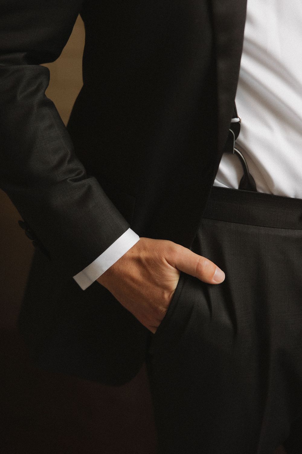 Close-up of hands in black suit jacket pockets showing professional business attire details.