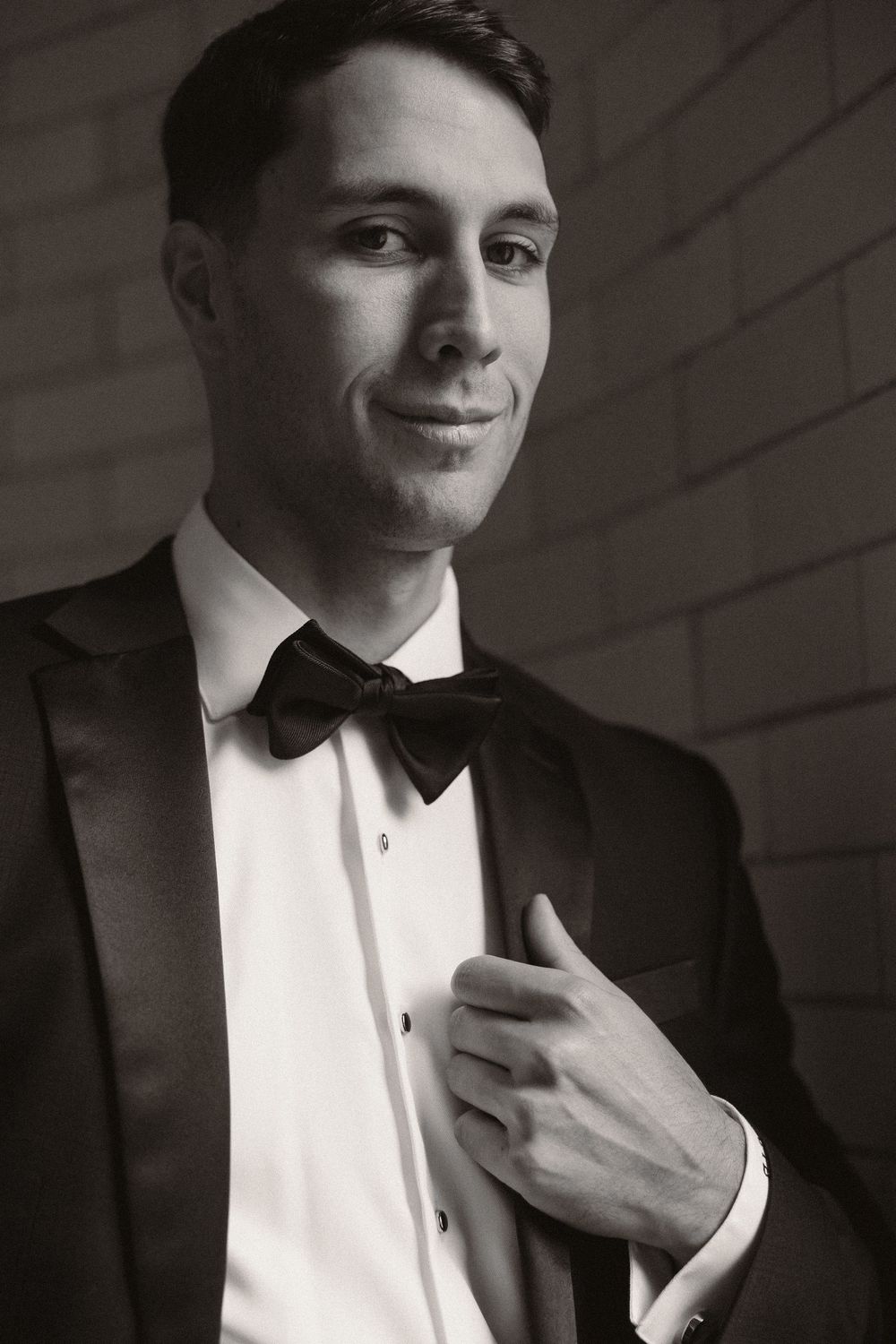 Classic black and white portrait series showing a man in a tuxedo adjusting his bowtie in dramatic lighting.