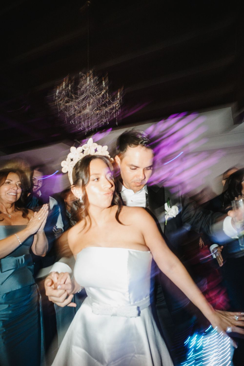 Wedding reception dance floor scene with motion blur and purple lighting effects showing people dancing.