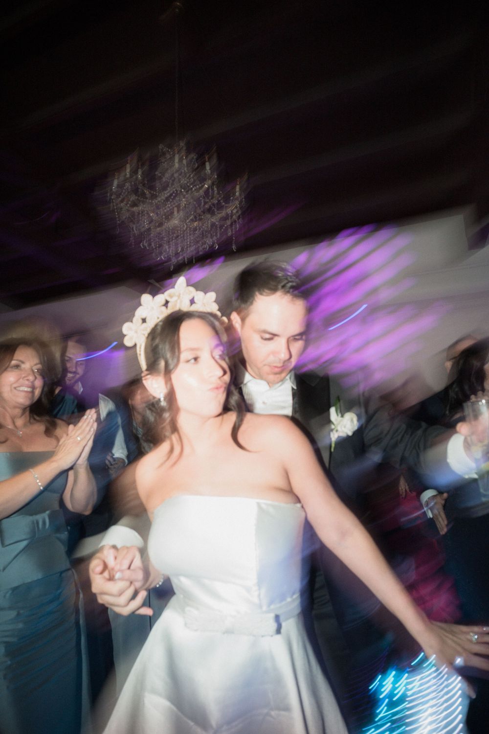 Bride in white strapless gown and floral crown dances with groom in tuxedo at wedding reception.