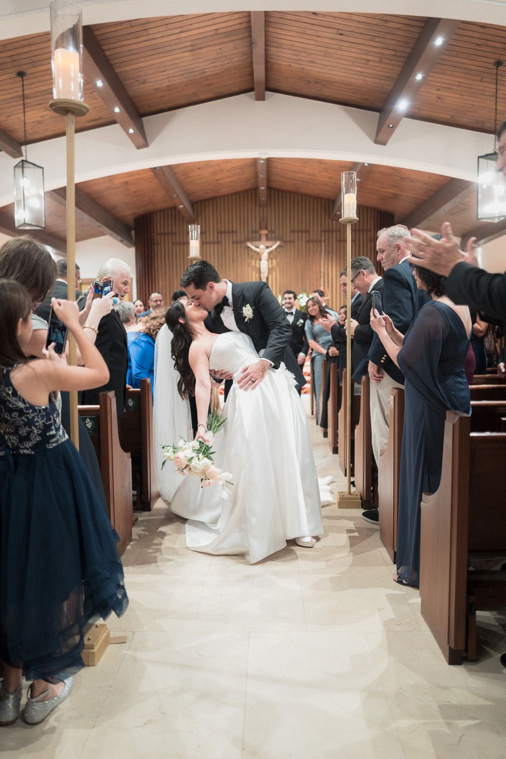 Bride and groom share a romantic dip kiss while walking down the church aisle after their wedding ceremony.