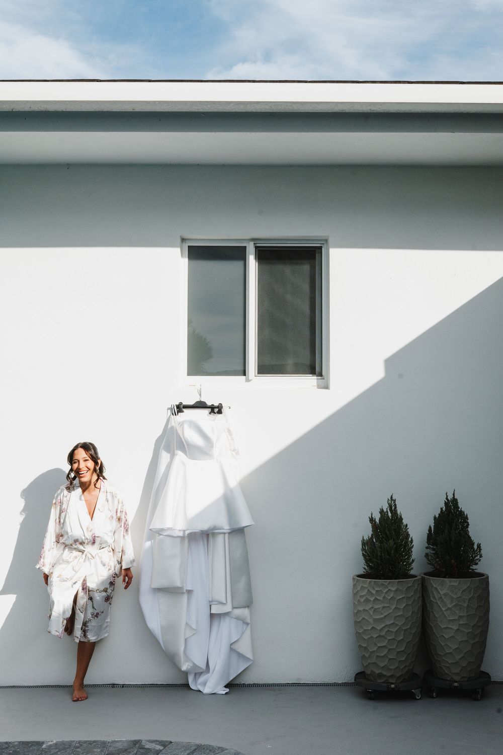 A minimalist photo series showing white clothing against a stark white wall with dark planters creating a modern aesthetic.