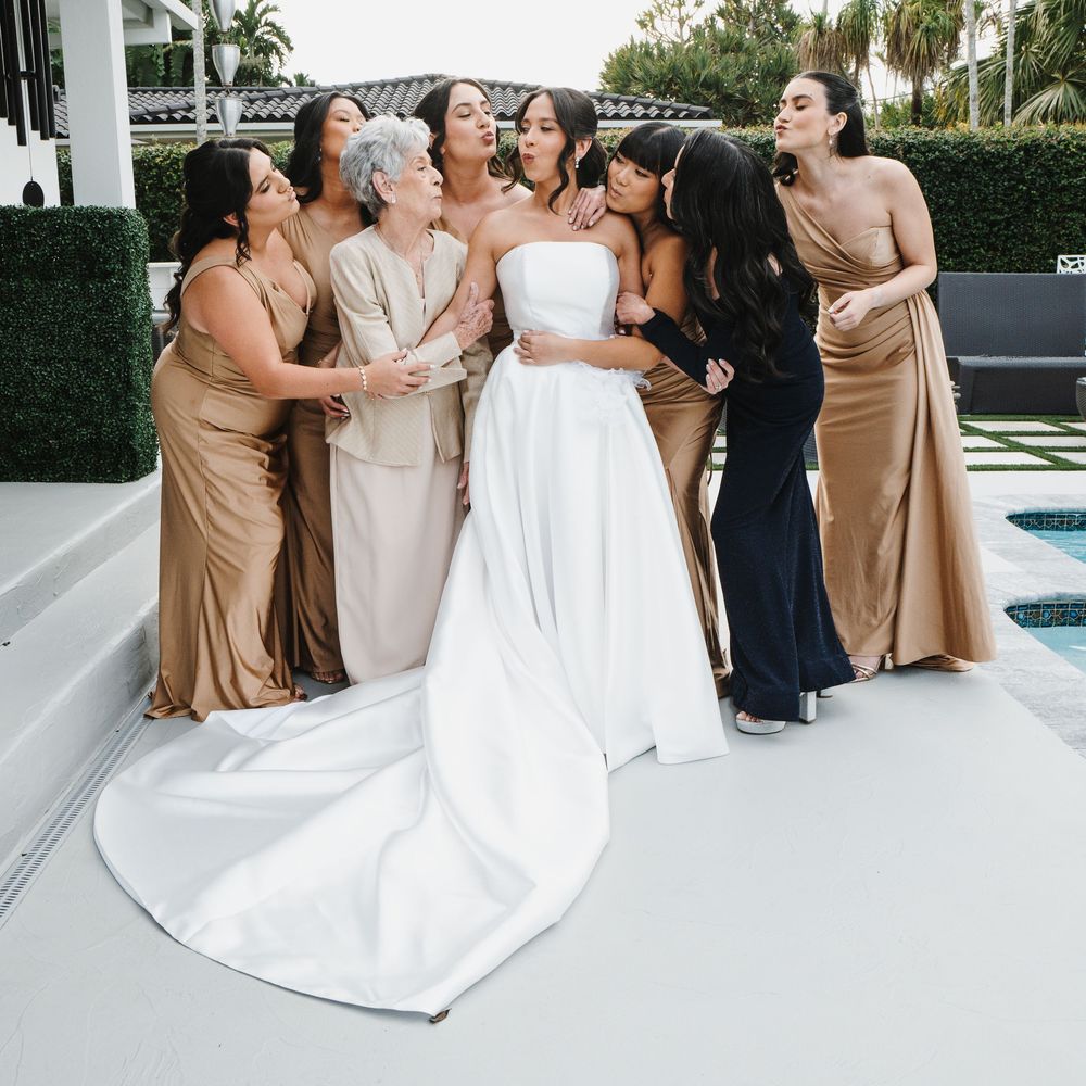 Wedding party in gold and white dresses pose together outdoors by a pool for formal photos.