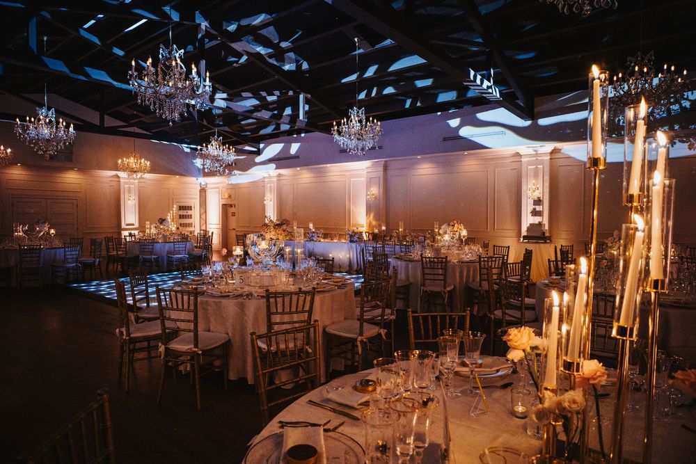 Elegant wedding reception ballroom with crystal chandeliers, candlelit tables, and dramatic blue ceiling lighting.