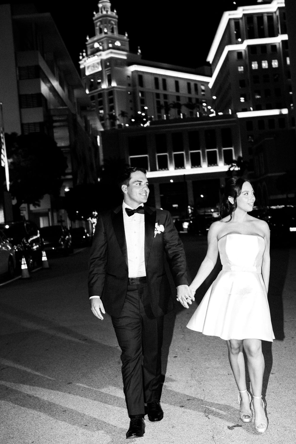 Black and white photo sequence shows a couple walking at night, with her white dress flowing in the city lights.