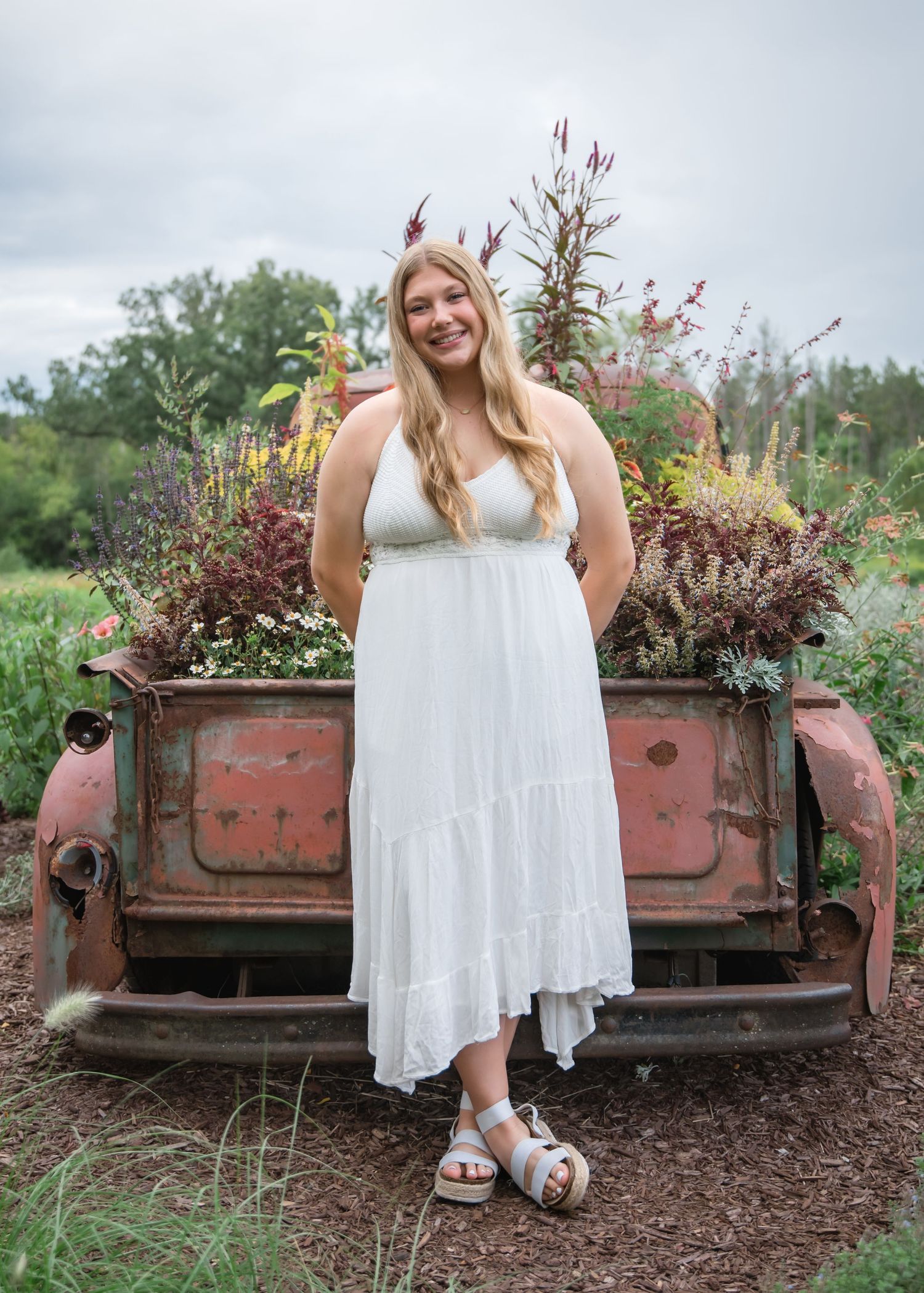 Rustic outdoor photo session featuring a white lace dress against vintage red truck bed filled with flowering plants.