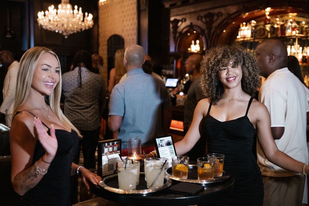 People mingling at an elegant evening event with crystal chandeliers and warm lighting in a luxurious venue.