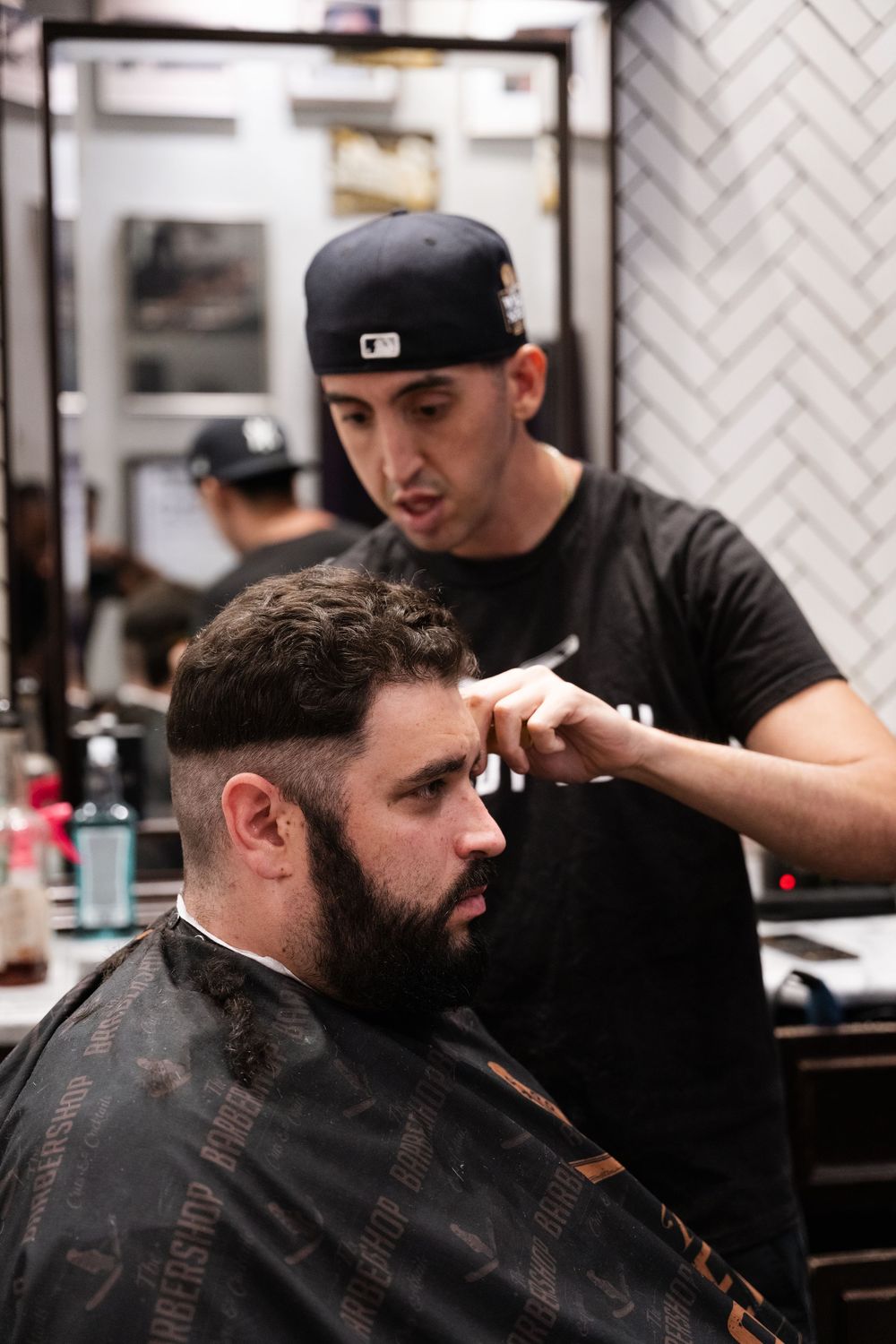 Professional barber giving a precise haircut to client in modern barbershop with dark interior.