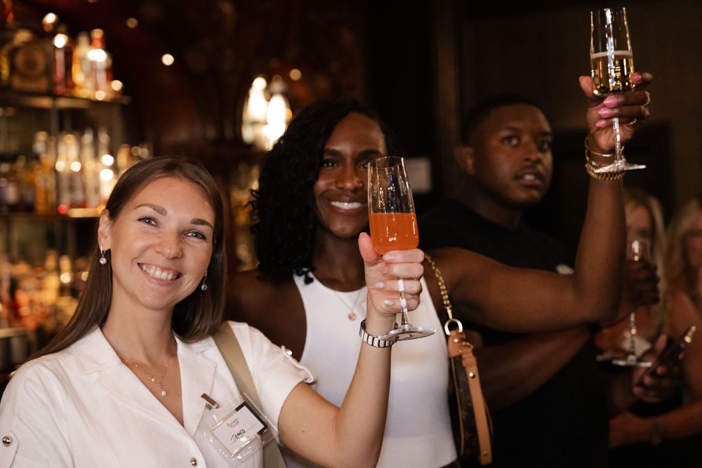 A group of diverse people enjoy drinks and conversation at a dimly lit bar.