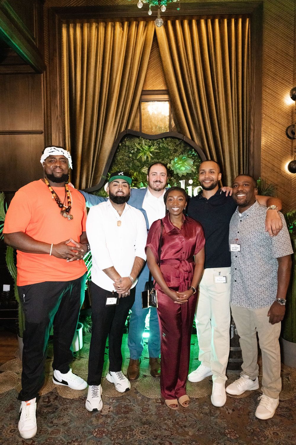 A group of friends pose together at an event with gold curtains and green lighting in the background.