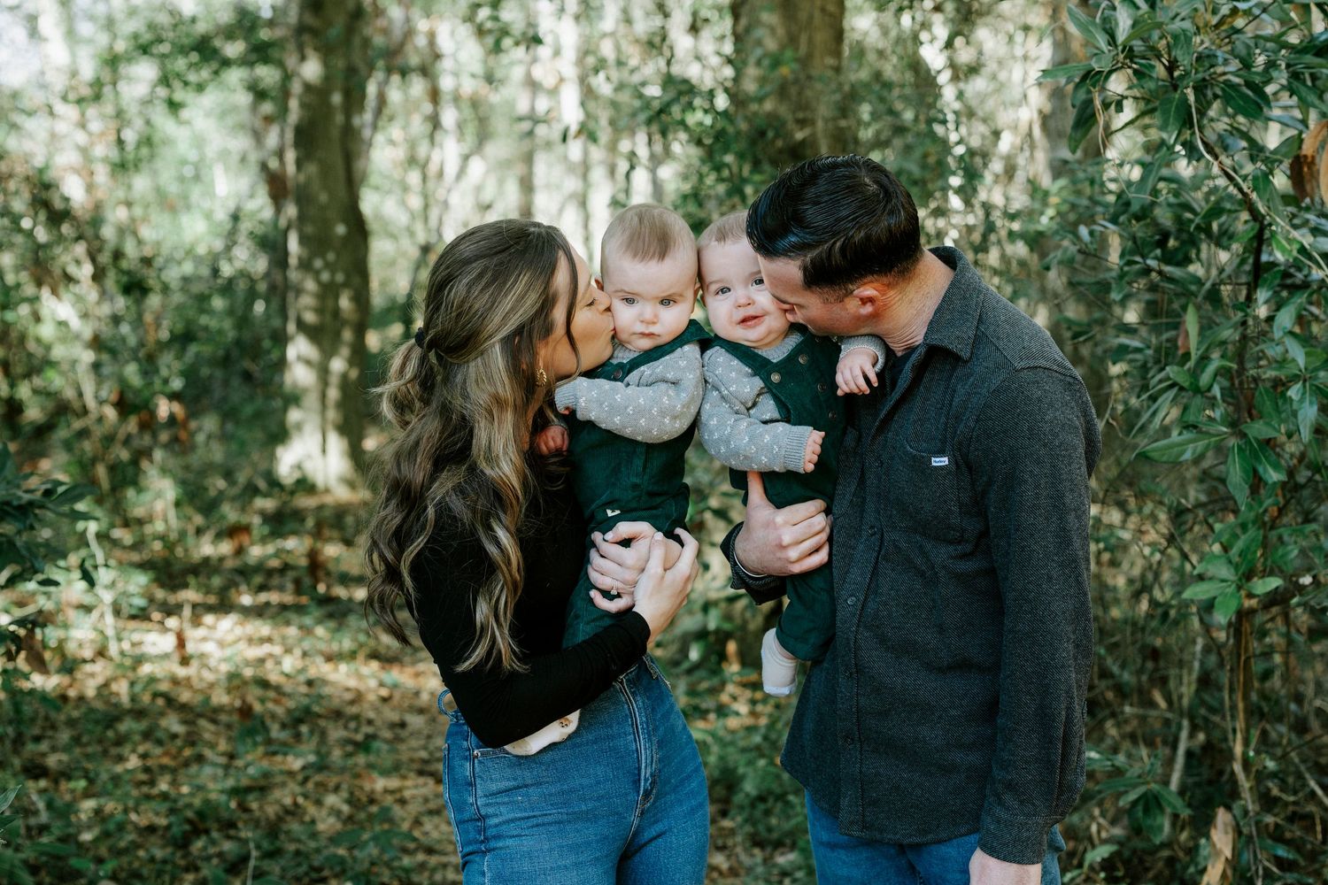 Family enjoying a tender moment together in a lush green forest setting.