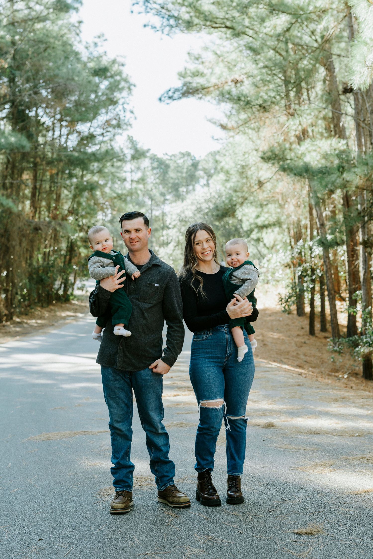A family in matching black and blue outfits walks together on a tree-lined path in a forest setting.