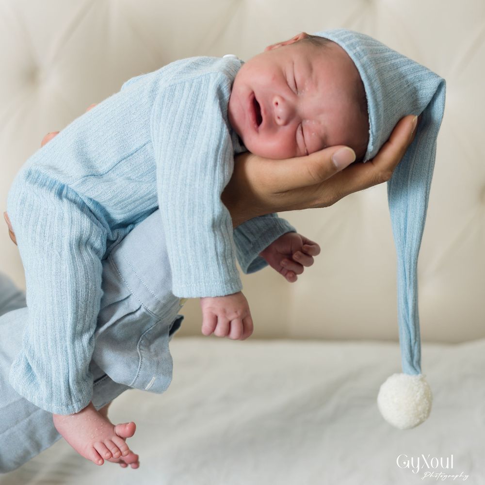 Newborn baby in light blue outfit lying on cream blanket shown in multiple artistic poses.