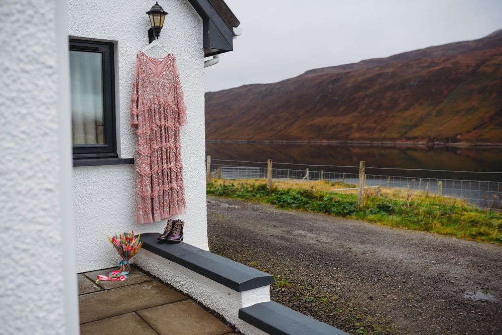 A rustic white cottage with a lantern sits along a remote Scottish highland road with mountains in the background.