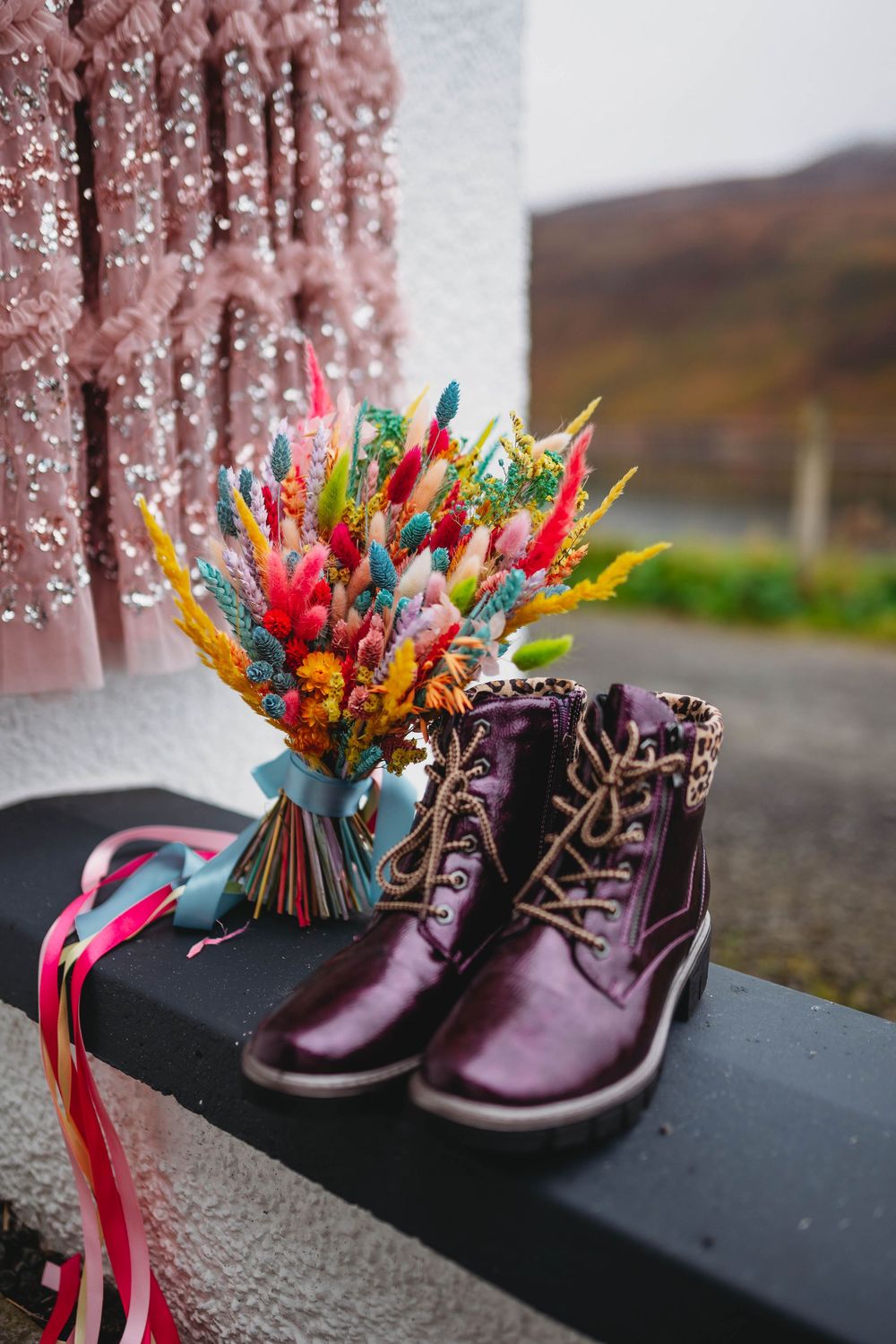 Small brown leather boots decorated with colorful origami paper cranes and ribbons displayed against a blurred background.